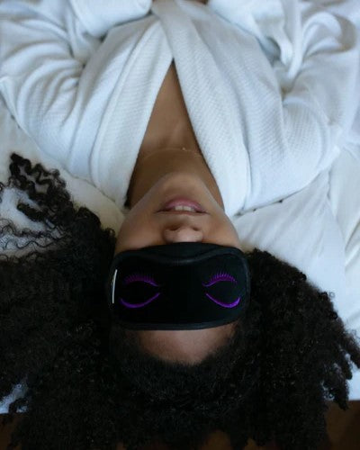 Woman lying on bed wearing robe and eye mask