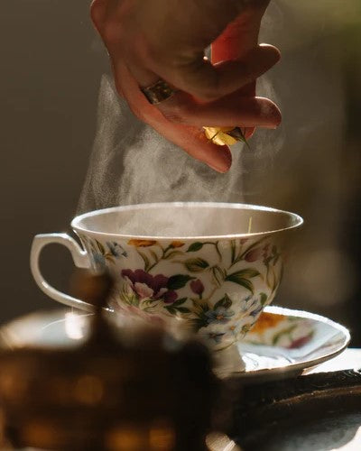hand dropping florals into steaming cup of tea