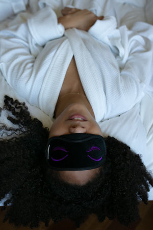 Woman lying on bed wearing robe and eye mask