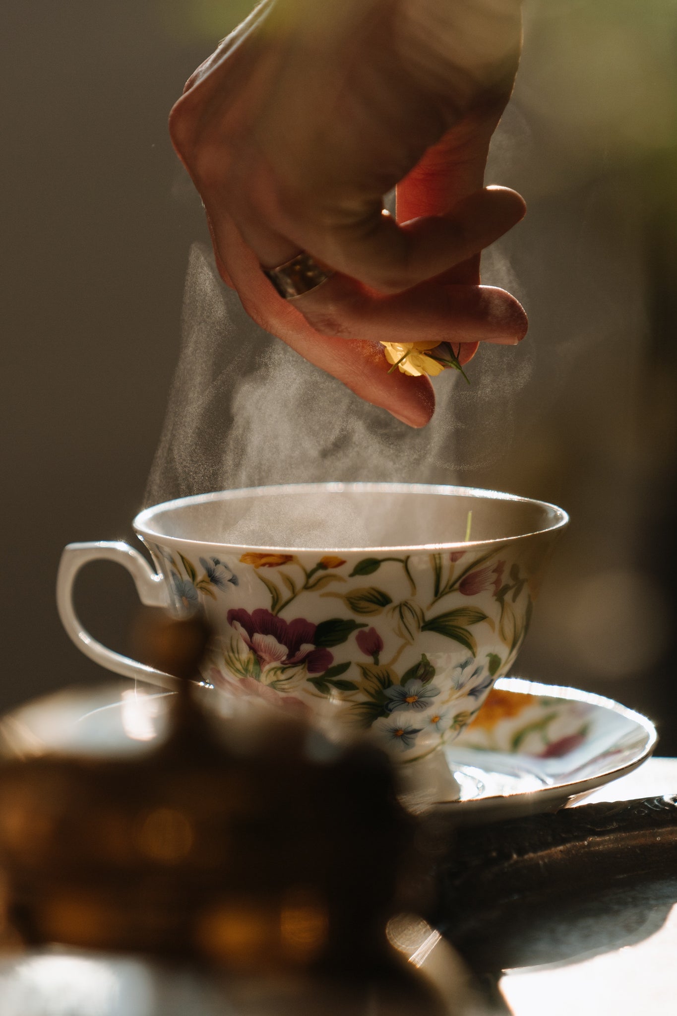 hand dropping florals into steaming cup of tea