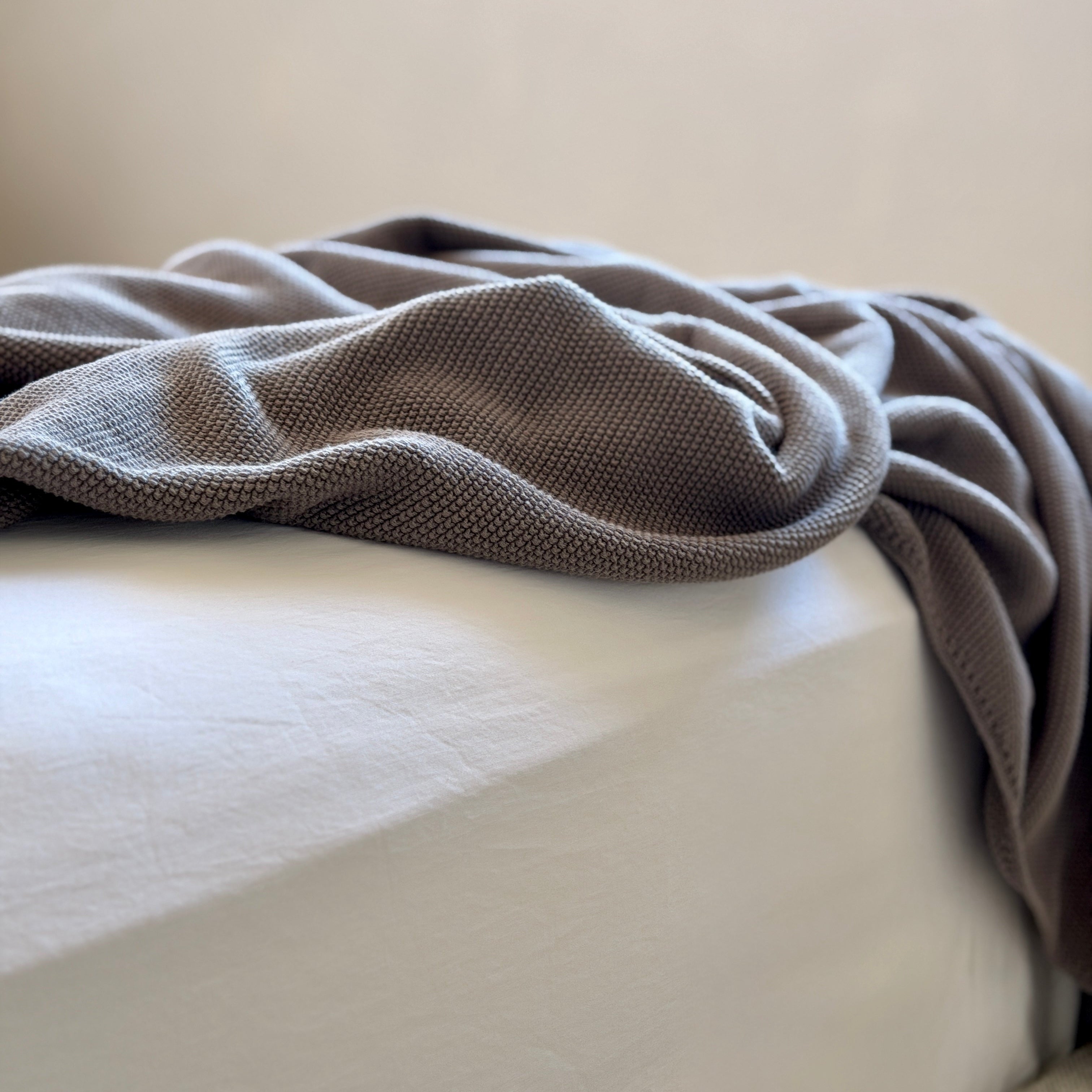 Gray blanket draped over a white surface with a neutral background